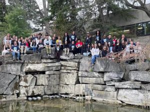 A large group of people stands at the edge of a rock wall with water below.
