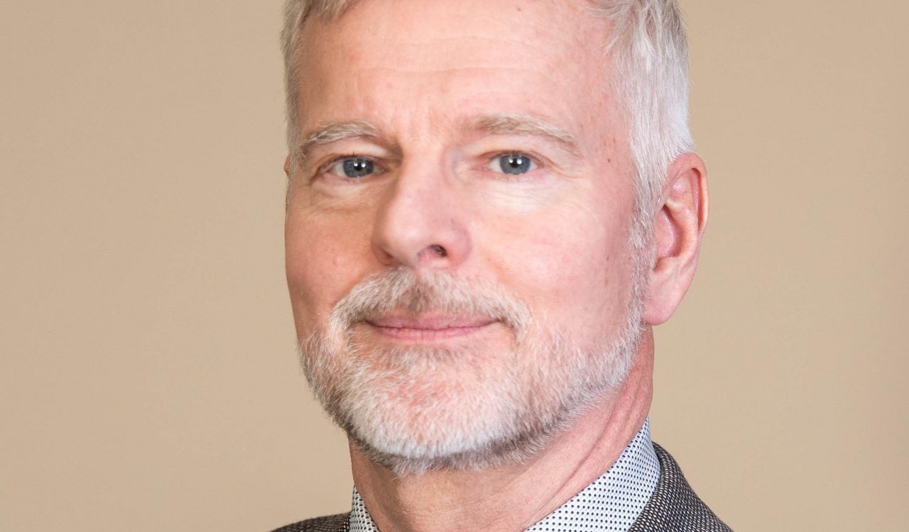Headshot of man in suit in front of beige wall.