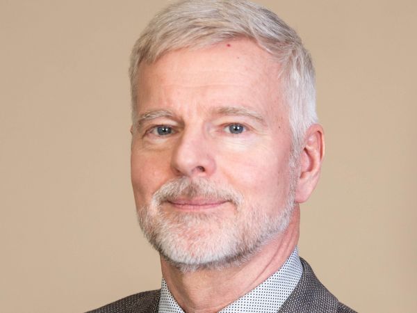 Headshot of man in suit in front of beige wall.