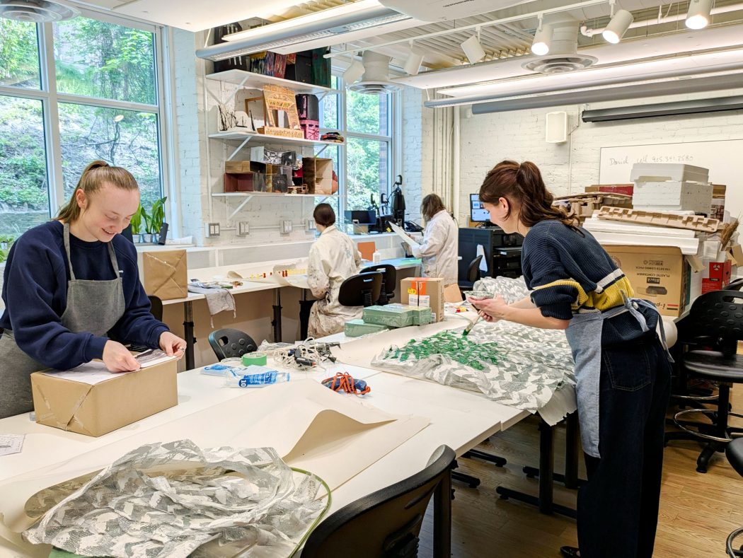 Four people paint and work on a 3D topographical map in a university art studio.