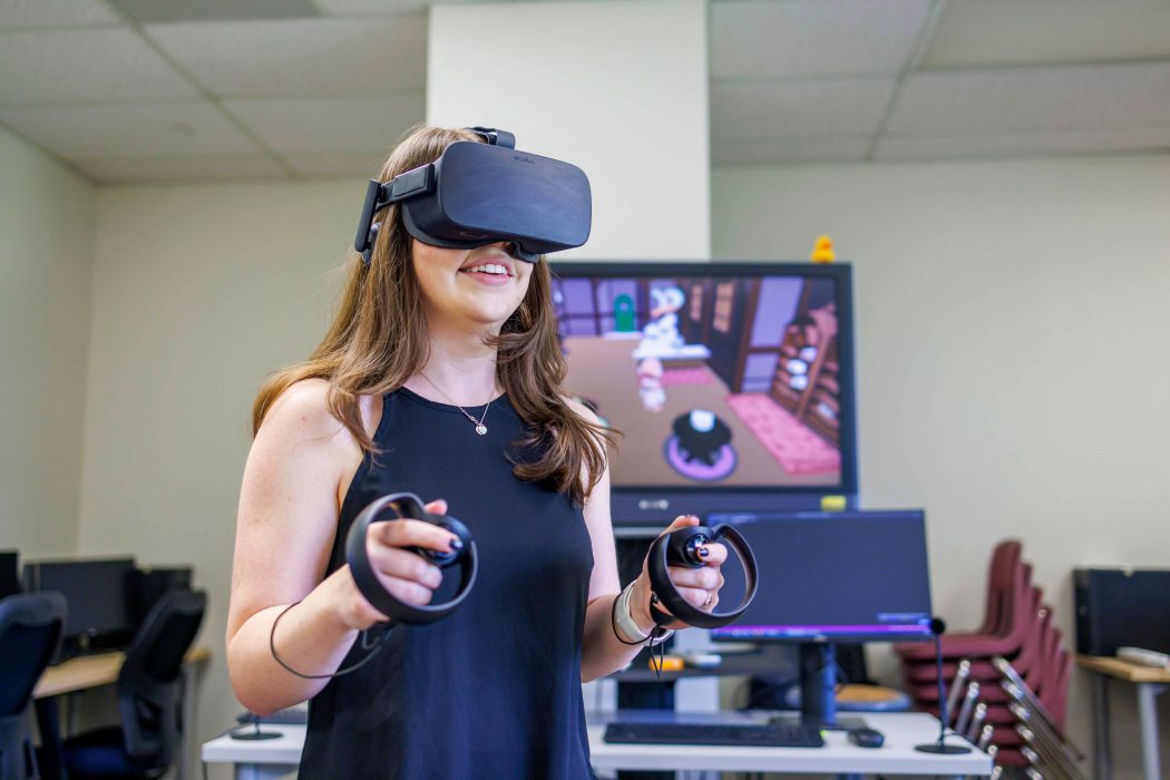 A young woman plays a video game using a VR headset and controllers. 