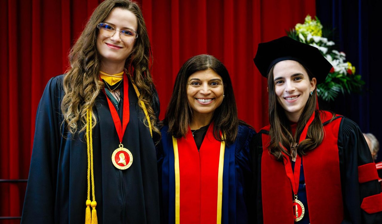 Three people in convocation gowns stand together, two wearing medals around their necks.