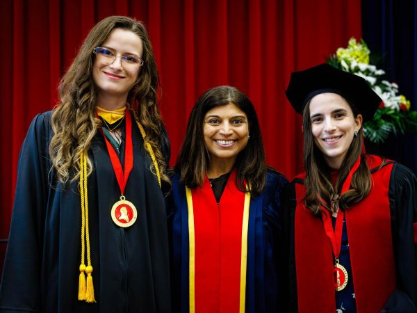 Three people in convocation gowns stand together, two wearing medals around their necks.