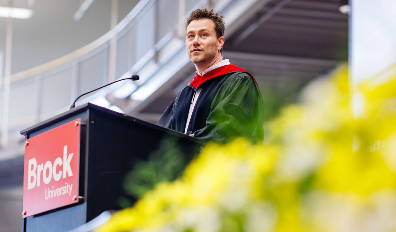 A man in a Convocation gown stands at a podium.