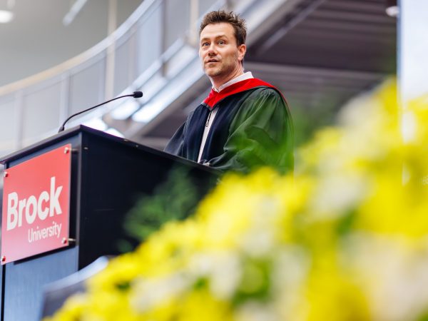 A man in a Convocation gown stands at a podium.
