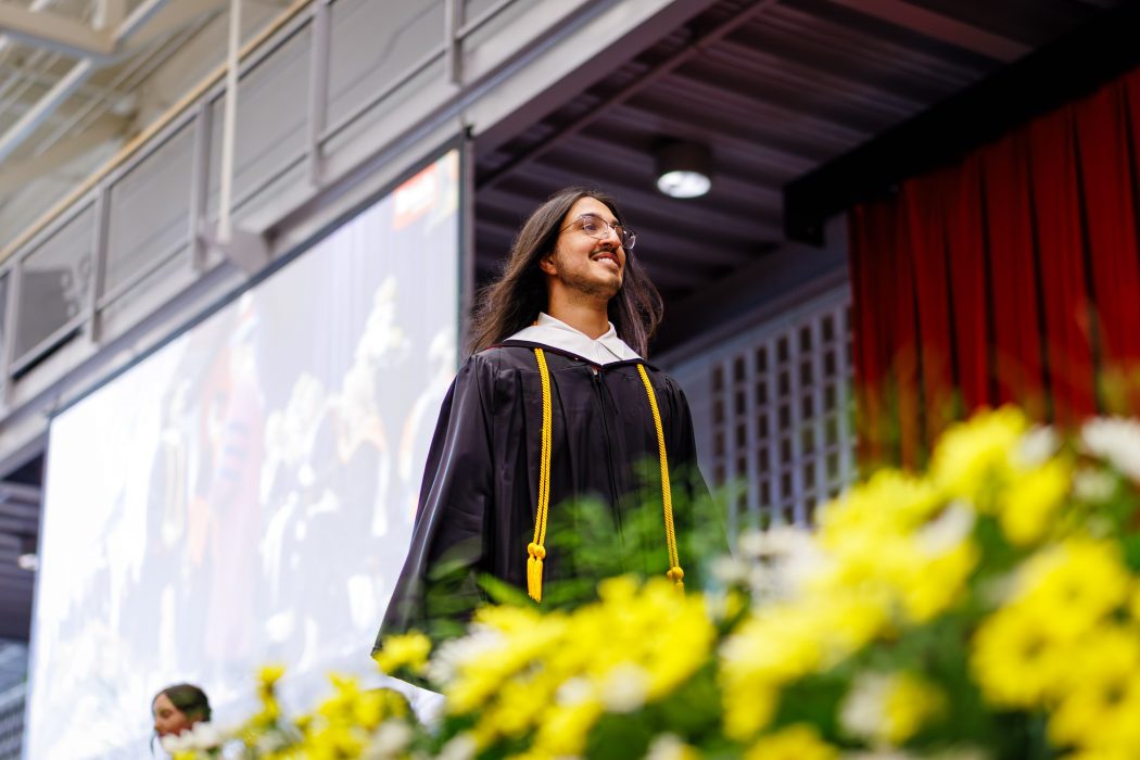 A man in a Convocation gown walks across the stage at graduation.