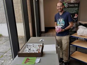 A man stands over a table filled with large photos of butterflies with paper descriptions below.