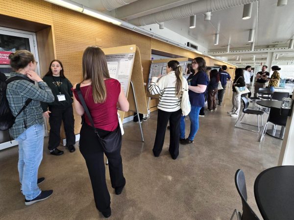 People look at research posters set up on easels in a hallway while speaking with one another.