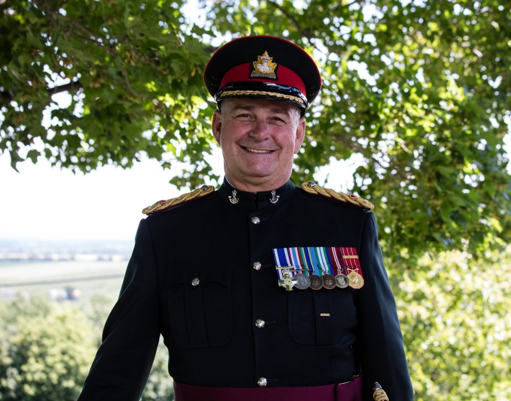 A man in a military outfit stands outside.