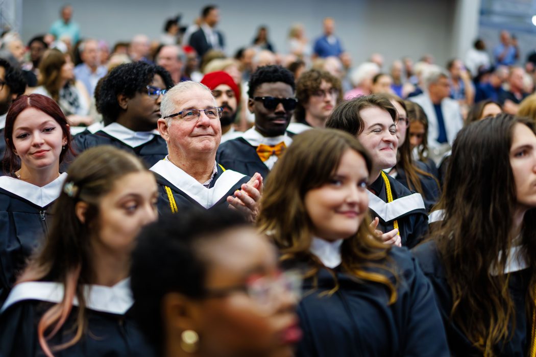 A gymnasium filled with graduating students in Convocation gowns look on.