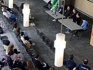 A panel of speakers sit at the front of a room in front of an audience.