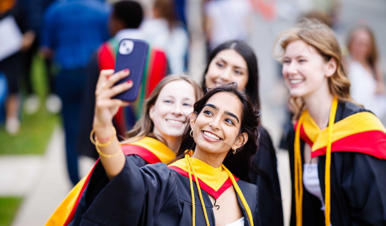Four young women in university graduation gowns pose for a selfie.