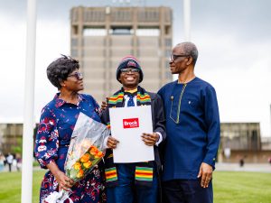 Parents look on over their child who is in a Convocation gown standing outside.
