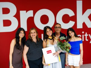 A family poses in front of a Brock University branded wall.