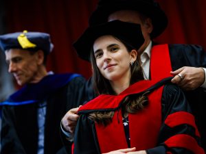A woman in a Convocation gown has a hood place over her head.