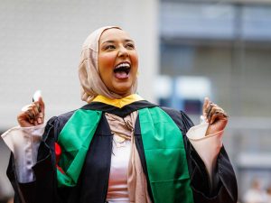 A woman in a convocation gown smiles.