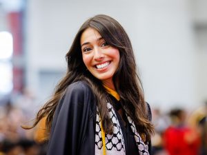 A woman in a convocation gown smiles.
