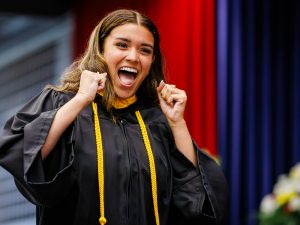A woman in a Convocation gown cheers on stage.