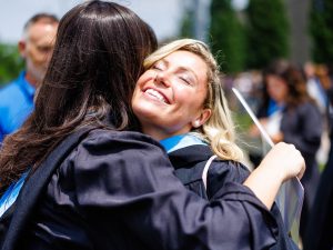 Two people in Convocation gowns hug outside.