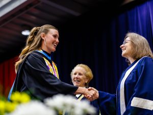 A graduate shakes the hand of a university president while crossing the Convocation stage.