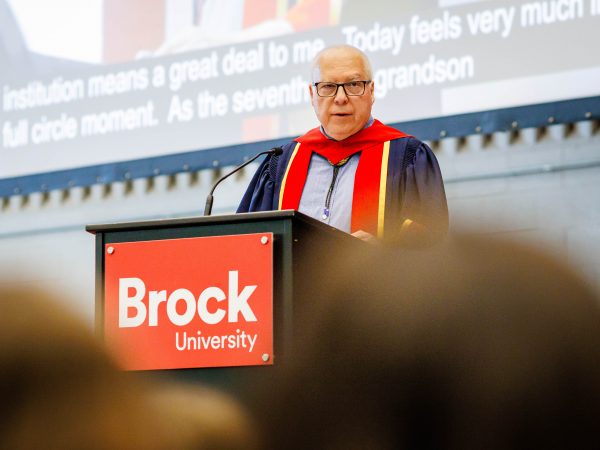 A man in a Convocation gown stands at a Brock University branded podium.