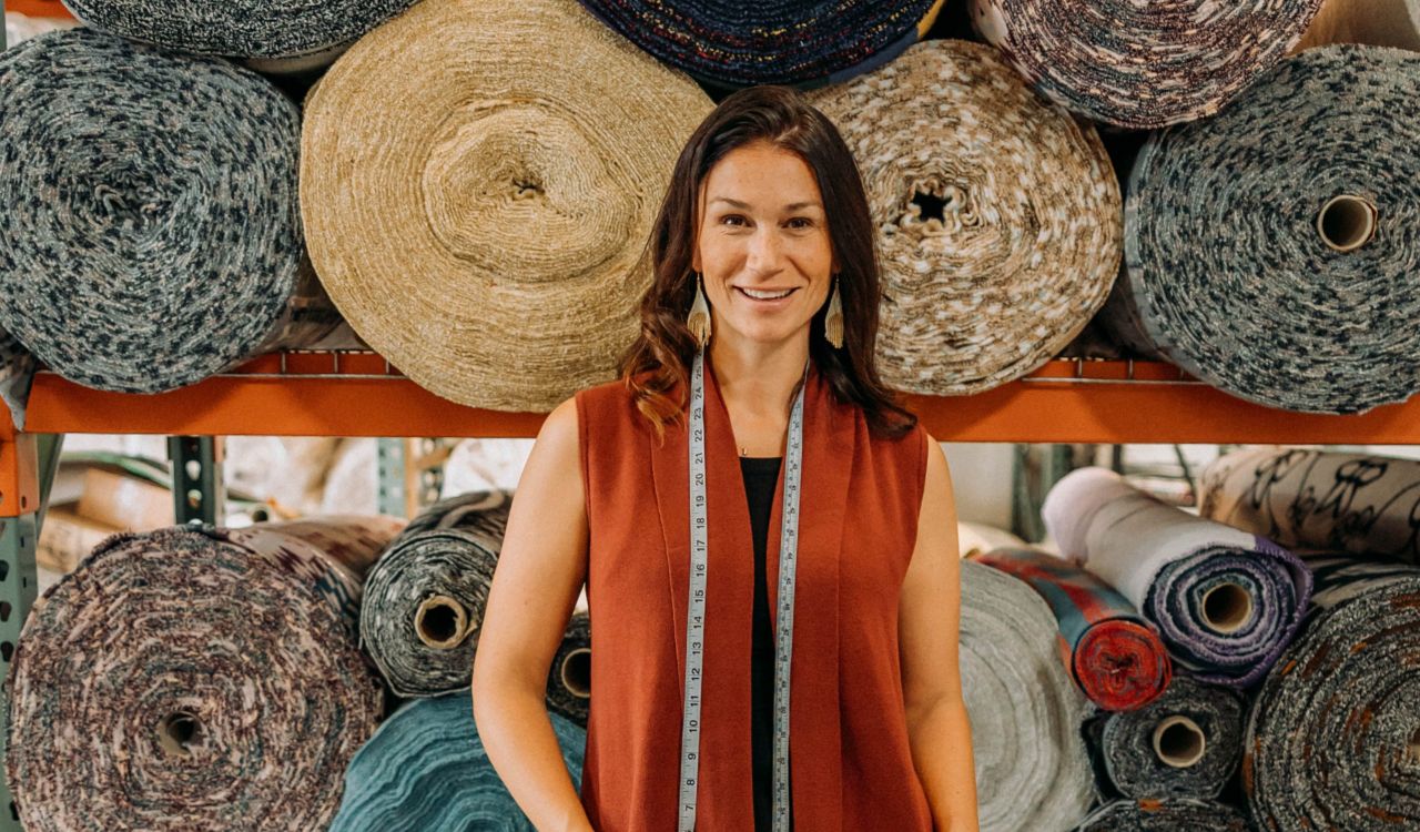 A woman poses in front of large rolls of fabric.