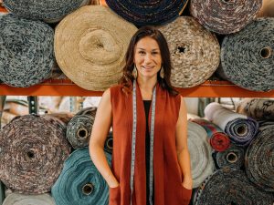 A woman poses in front of large rolls of fabric.