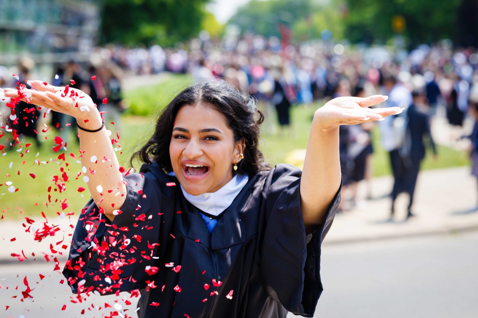 A young woman in academic robes throws confetti at a university graduation ceremony.