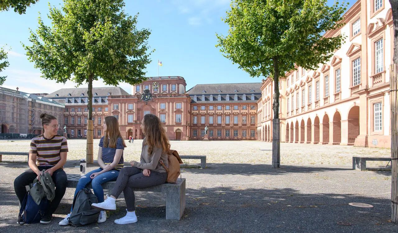 Three university students sit in a courtyard surrounded by old brick buildings.