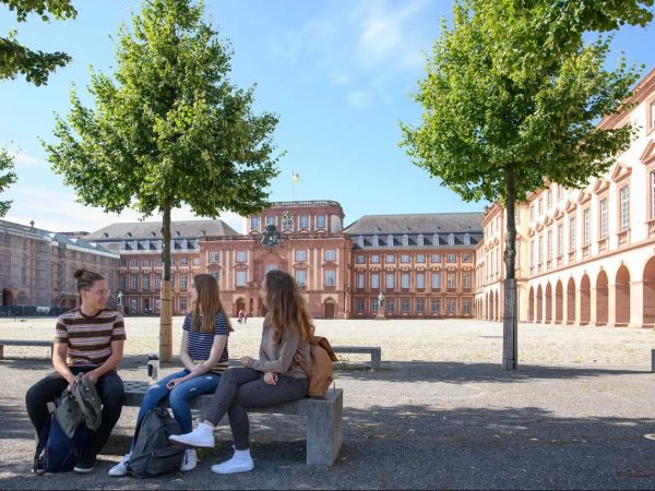 Three university students sit in a courtyard surrounded by old brick buildings.