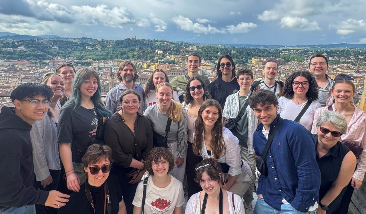A group of people stand atop Duomo Santa Maria in Florence, Italy with a view of the Florence behind them.