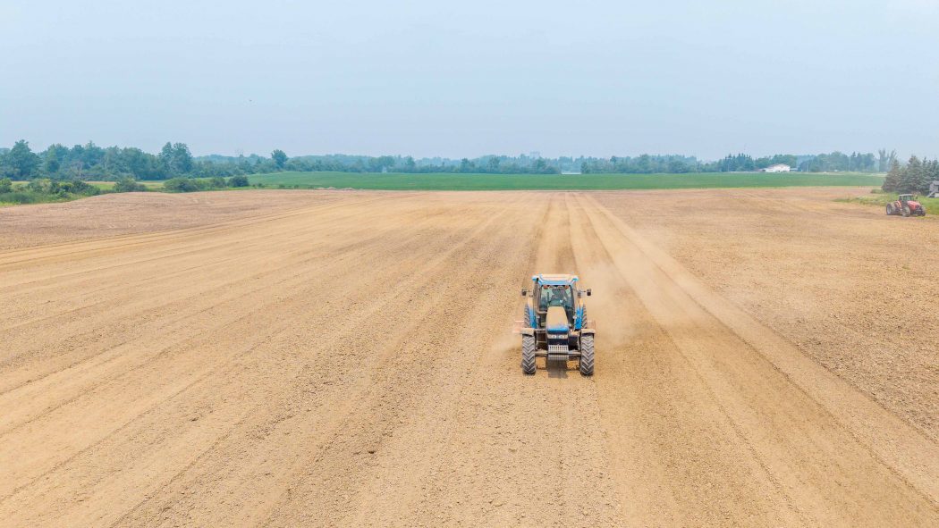 A tractor drives through a field with green trees in the background.
