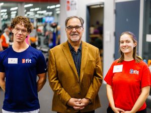 A man standing with 2 students in a gym where people are exercising.