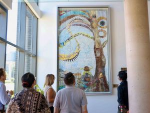 A group of people stand in front of a large framed quilt.