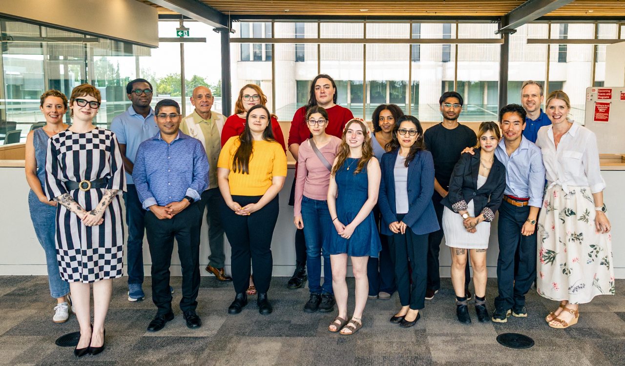 A large group of smiling people pose for a photo in a bright atrium at Brock University.