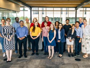 A large group of smiling people pose for a photo in a bright atrium at Brock University.