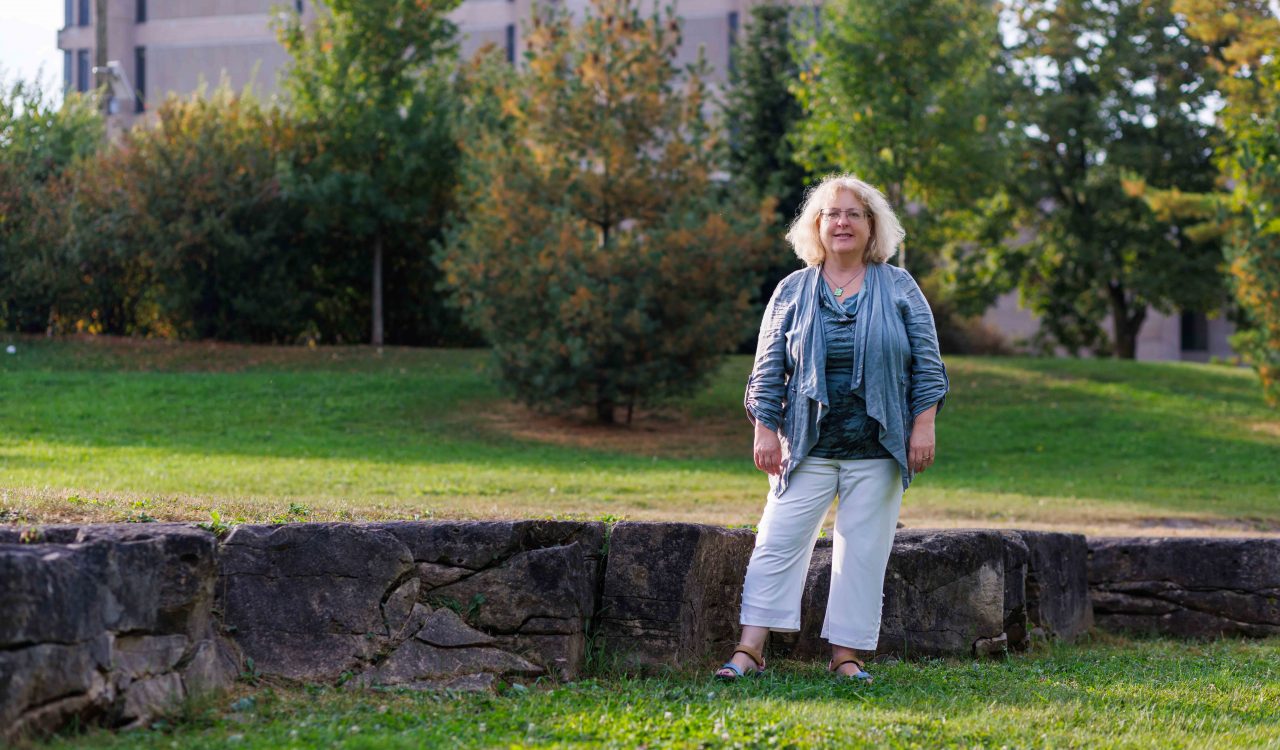 A woman poses for a photo while standing in a green space in front of a concrete tower.