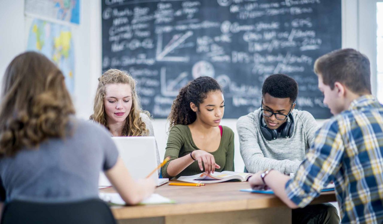 A group of high school students study together at a table in a classroom.
