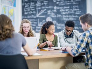 A group of high school students study together at a table in a classroom.
