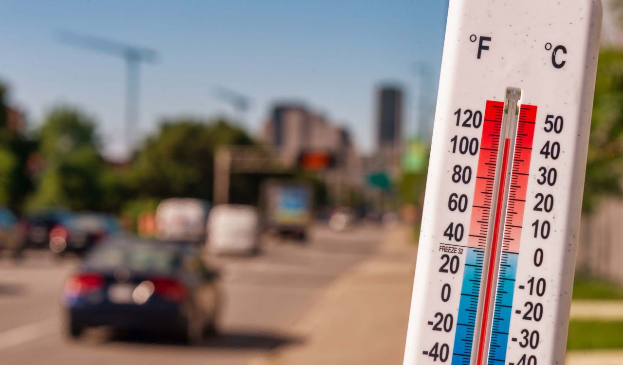 A thermometer showing high temperatures with cars and a busy street in the background.