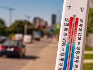A thermometer showing high temperatures with cars and a busy street in the background.
