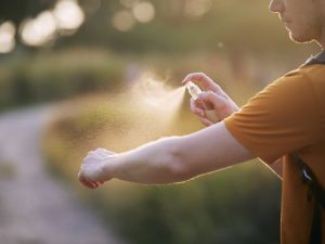 Man sprays bug spray on his body outdoors.