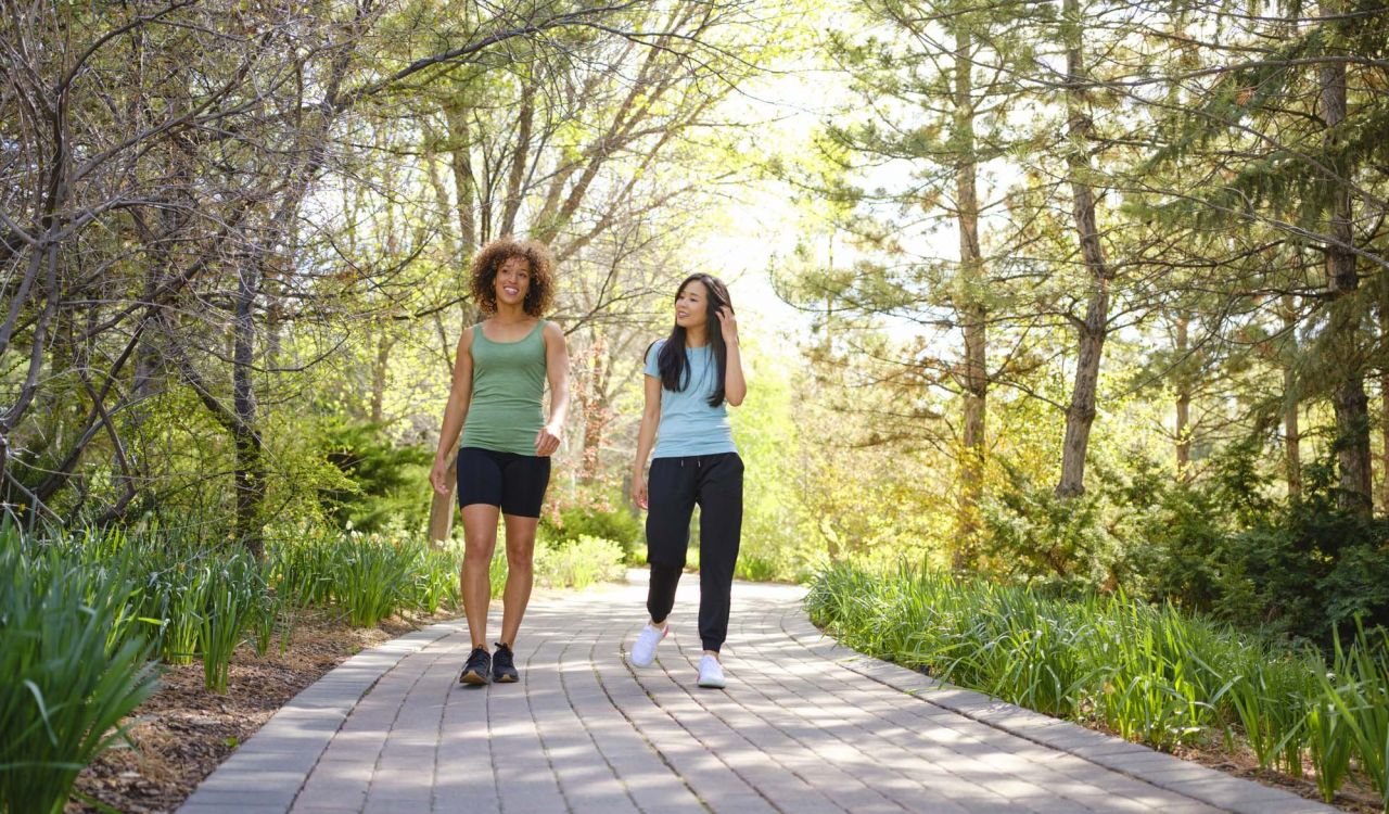 Two women walk along a path in a park while chatting.