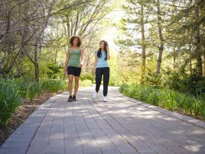 Two women walk along a path in a park while chatting.