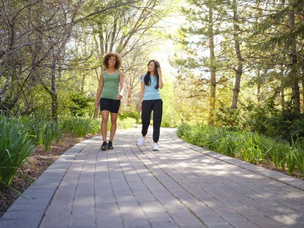 Two women walk along a path in a park while chatting.