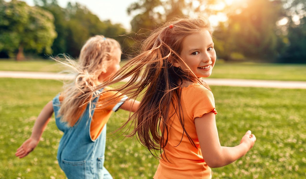 Two children run through a park on a sunny day.