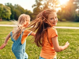 Two children run through a park on a sunny day.