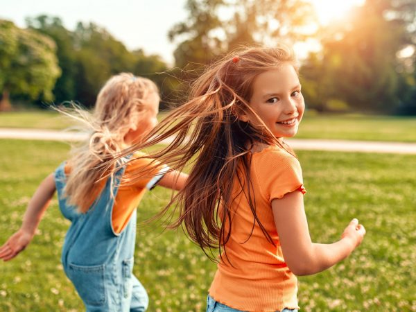 Two children run through a park on a sunny day.