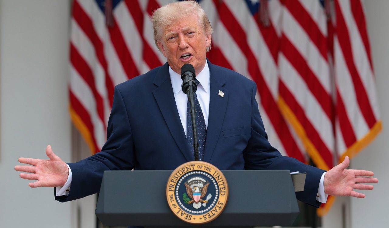 U.S. President Donald Trump stands at a podium speaking with his hands raised out to his sides.