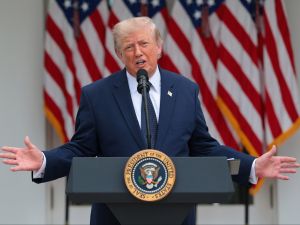 U.S. President Donald Trump stands at a podium speaking with his hands raised out to his sides.